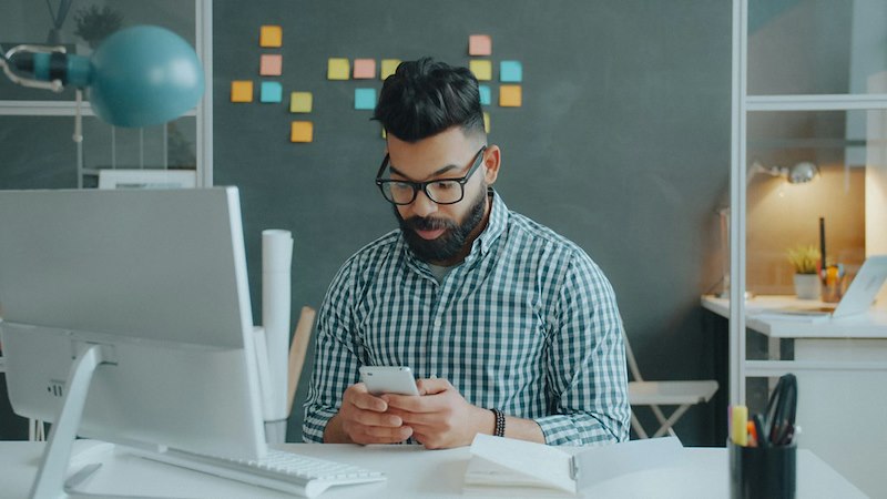 Employee checks his phone at work after learning his company is eliminating his role.