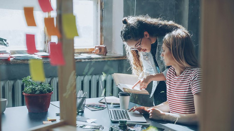 Two women collaborate over a laptop