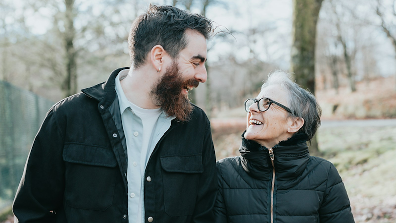 A man walks with his mom through a park during fall.
