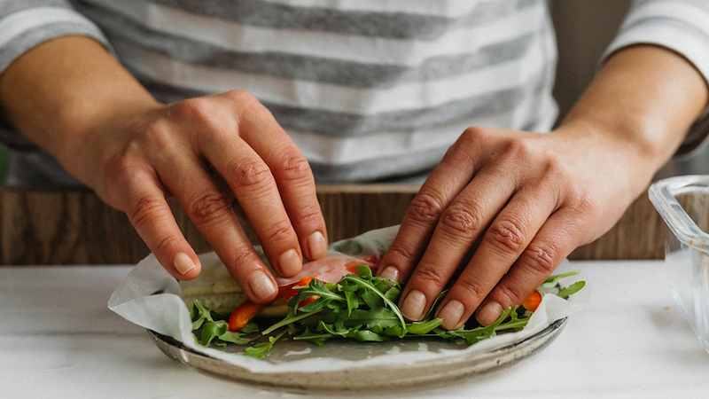 Close-up of hands wrapping vegetables in rice paper.