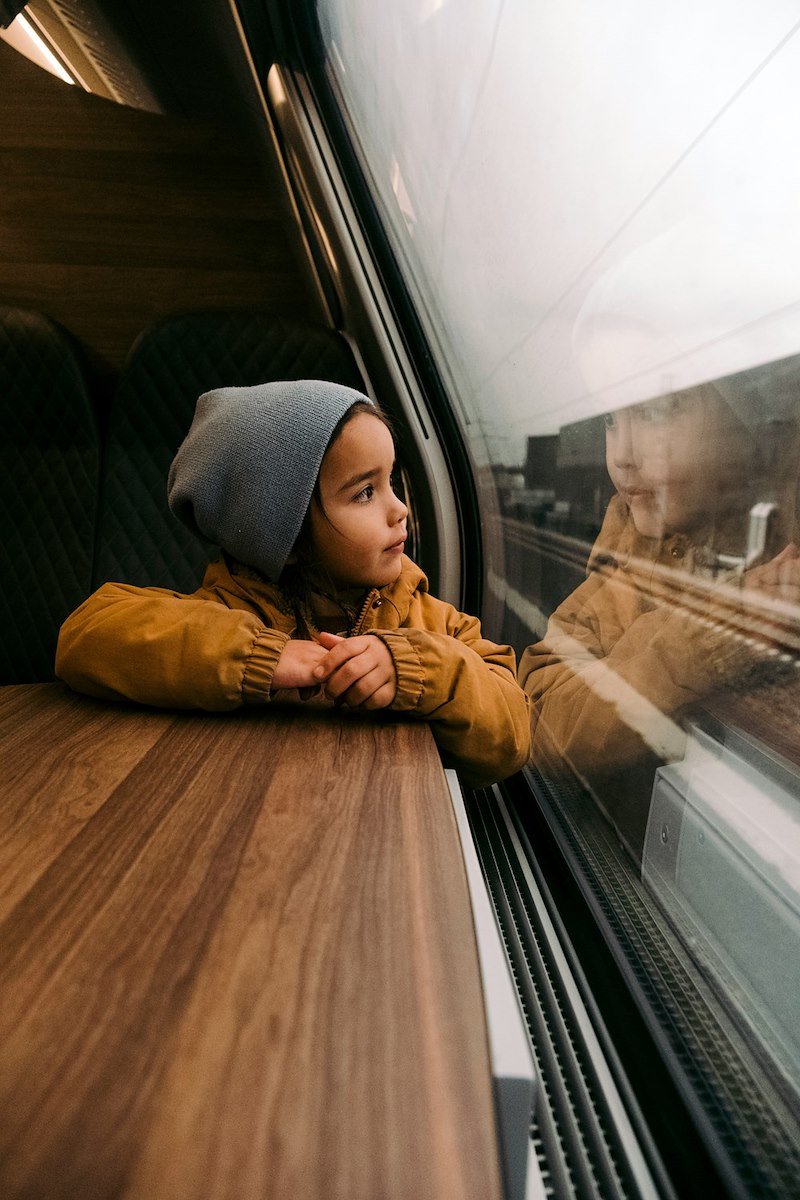 A young girl sits by a train window during a journey.