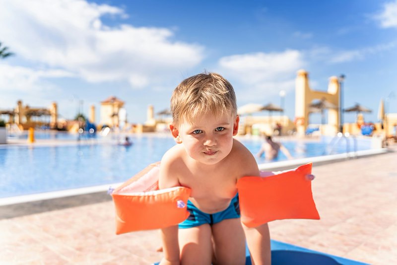 Young child stands beside a hotel swimming pool.