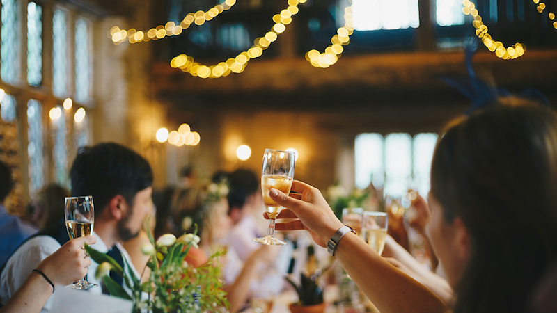 People sitting at a table, raising a toast at a rehearsal dinner.