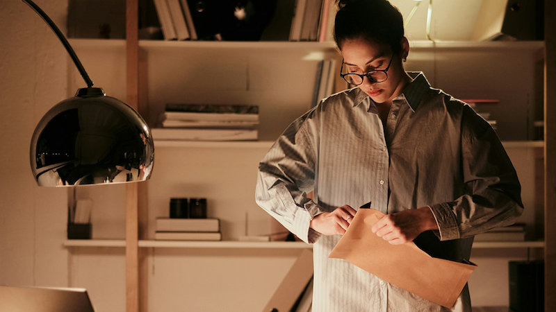 A woman closes a large brown envelope while standing in a personal office.
