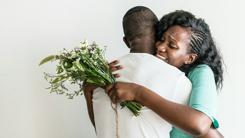 A woman hugs her boyfriend while holding a bunch of flowers.