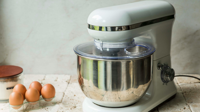 A white stand mixer sitting on a counter next to some eggs.