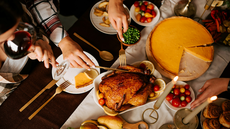 Overhead view of people serving themselves turkey and pumpkin pie at a Thanksgiving table.