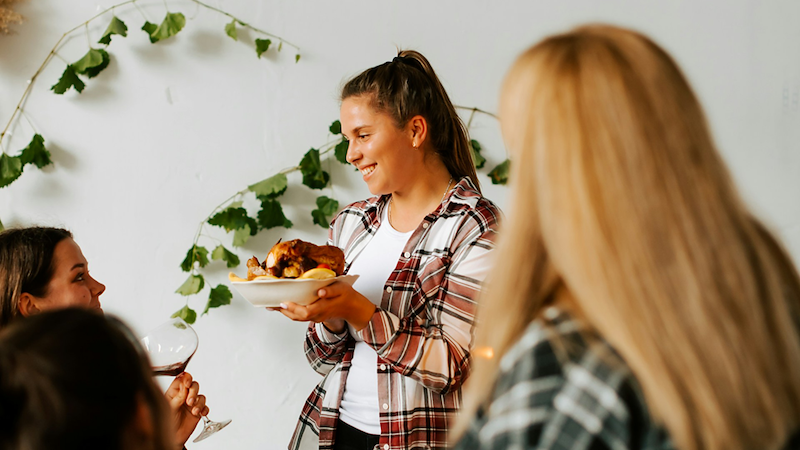 A woman talks with relatives while standing and holding a plate of turkey.