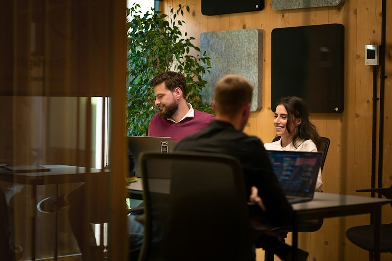 Two coworkers sit side by side at a desk at an office