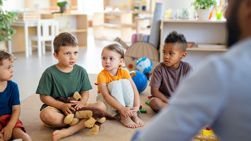 Four children sit in front of a male daycare assistant.