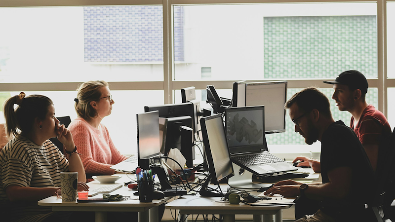 Four employees working at a shared desk by a window.