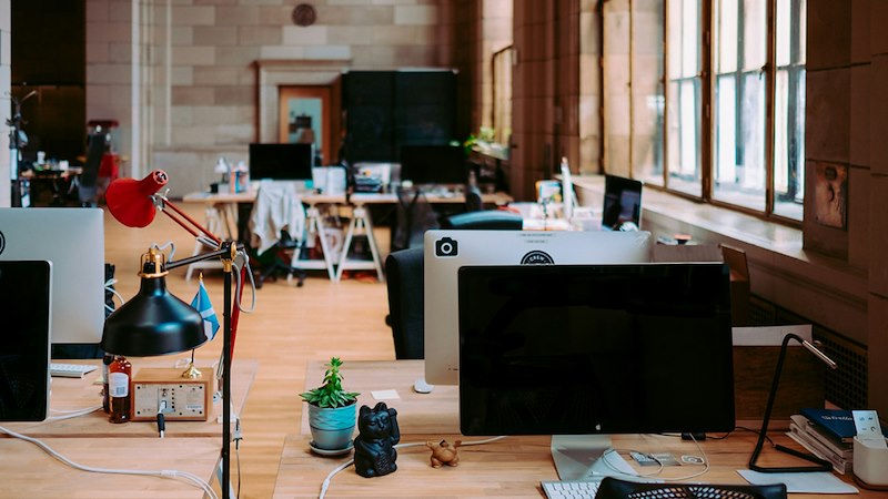 Computer monitors at empty desks in an open-plan office.