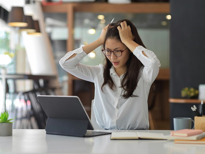 A stressed young businesswoman looks at her computer, upset