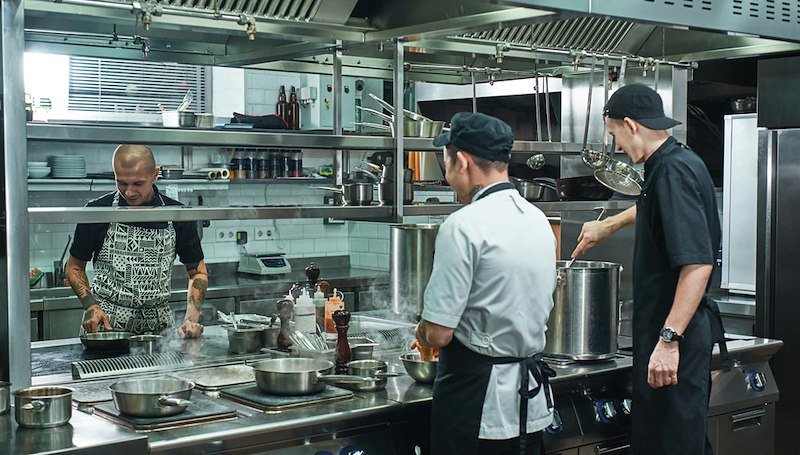 Restaurant employees working around hot stoves and cooking equipment in a commercial kitchen.