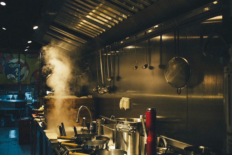 Steam rising from cooking equipment inside a restaurant kitchen.