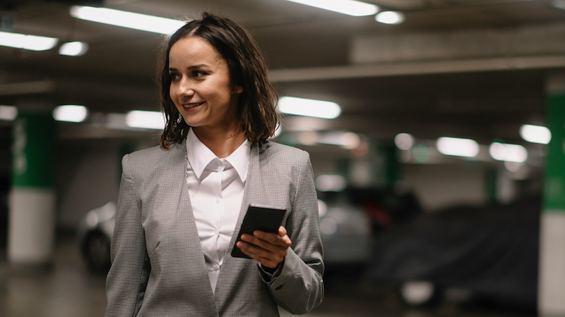 A job applicant looks to the side as she holds her phone in a parking garage.