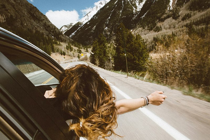 A woman on a road trip with her hair out of the window. Picture does not depict real parties.