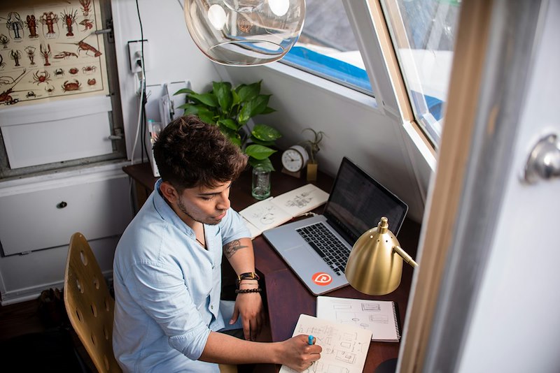 Remote employee working from his home office with a laptop and a notebook.