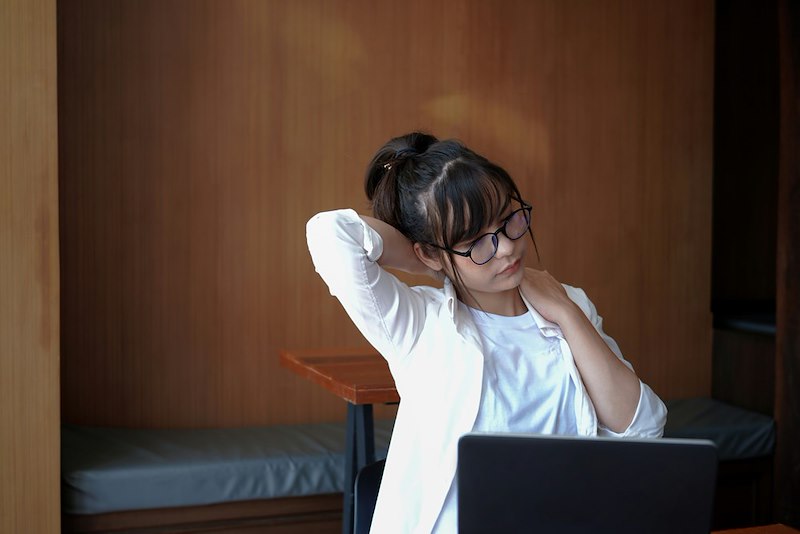 A female office worker rubs her shoulders at her desk