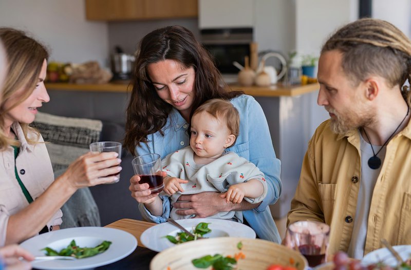 The guest brings the baby to his mom and lets her know the child needs a diaper change.