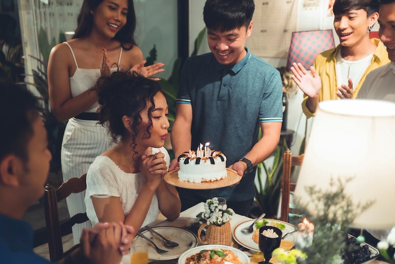 A friend is handed a birthday cake at their birthday dinner