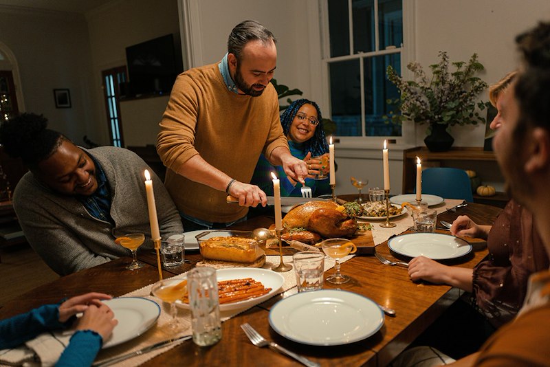A man carves a turkey at a thanksgiving table