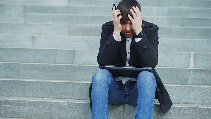 A man is upset, sitting on steps with head in hands