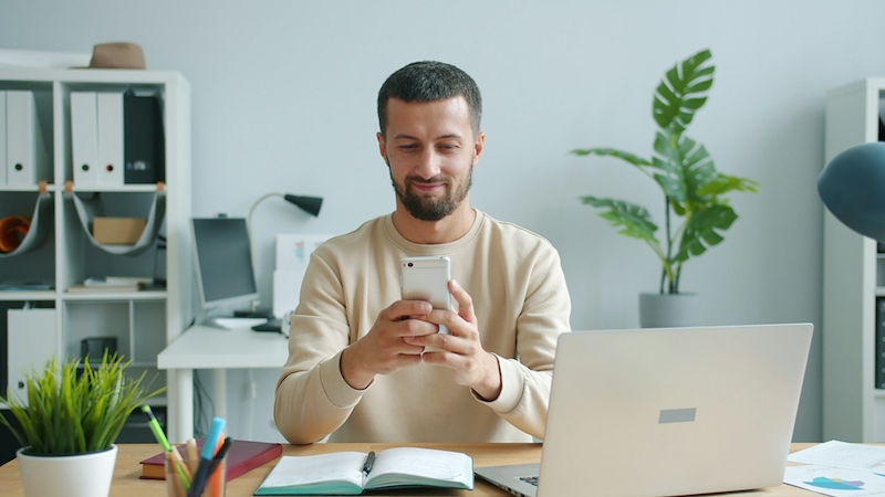 A boss sends a text while sitting at his desk.