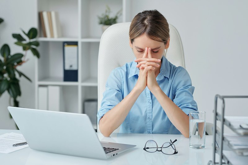 A frustrated employee puts her hands by her face at her desk