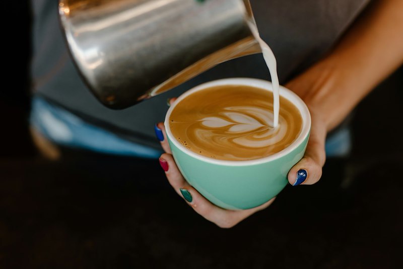 A barista pours milk in a latte