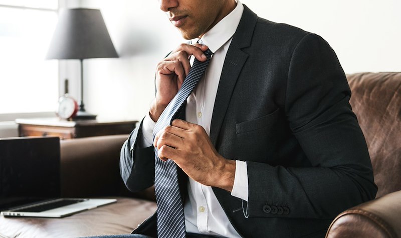 An employee adjusts his tie, wearing formal office wear