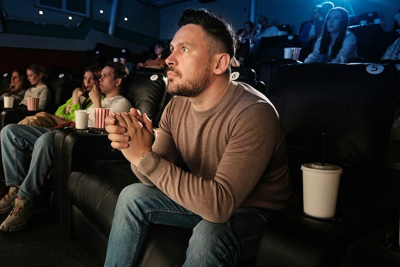 A man in a stand up comedy crowd leans on the edge of his seat
