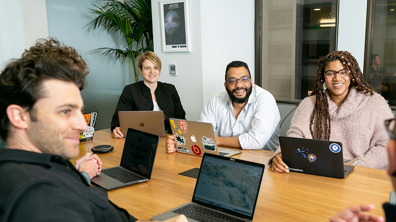 Employees sitting around a meeting table, listening to someone talk.