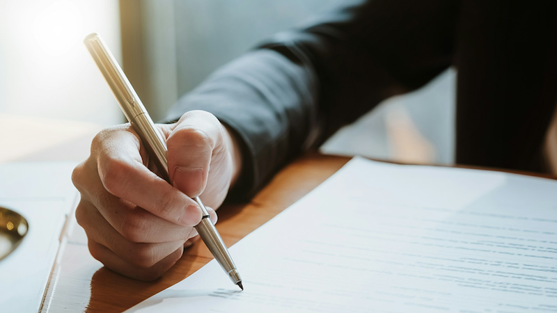 Close-up of a person signing a document on a clipboard.