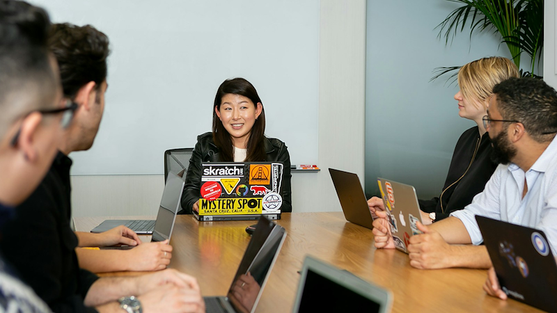 Employees sitting around a meeting table with their open laptops.
