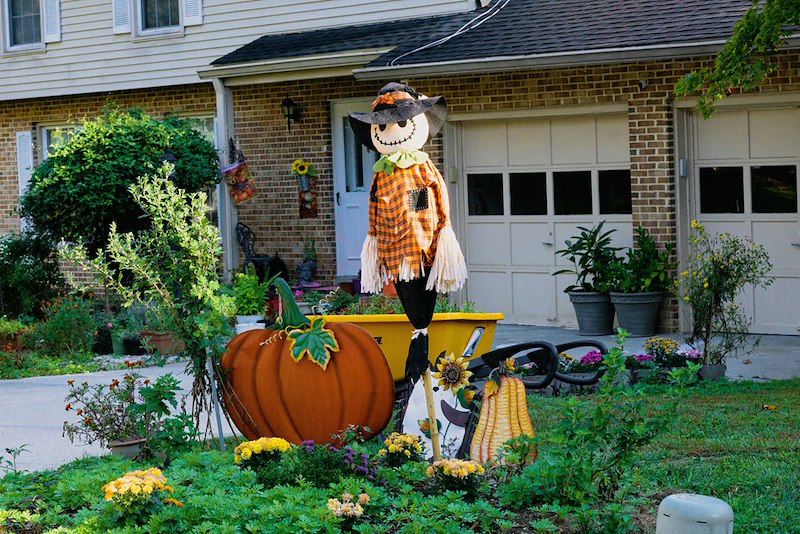 Halloween front yard decorations with a smiling scarecrow.