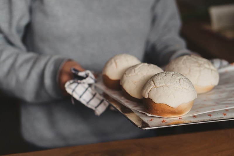 A woman takes a tray of pastries out of the oven