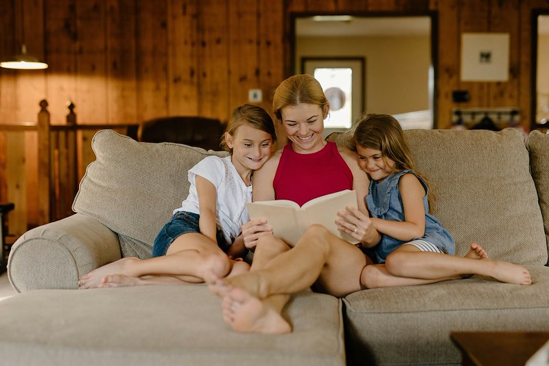 Aunt reading a book with nieces on a couch.
