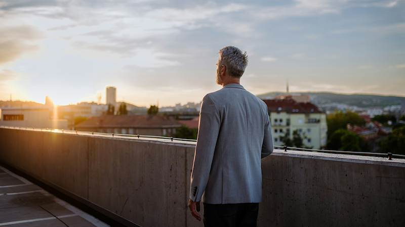The back of a businessman standing on a rooftop at sunrise.