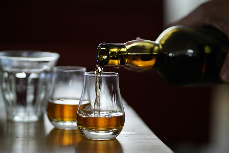 A person pours whiskey into two glasses