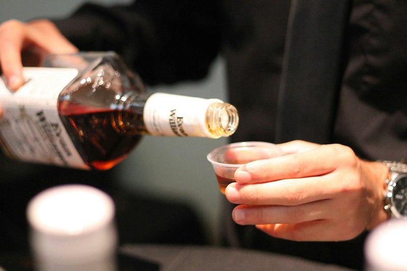 A person pours amber liquid into a small glass