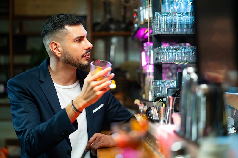 A man holds out a glass at a bar counter