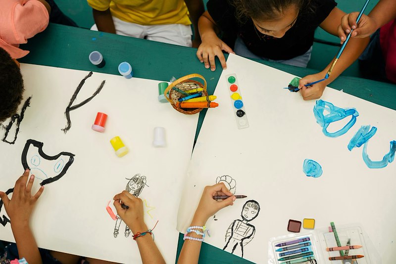 A group of children sit around with paint and craft supplies