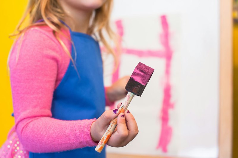 A girl uses a pink paint brush at a party