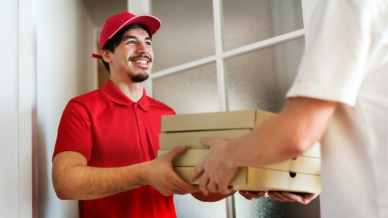 A pizza delivery guy hands several pizza boxes to a customer.
