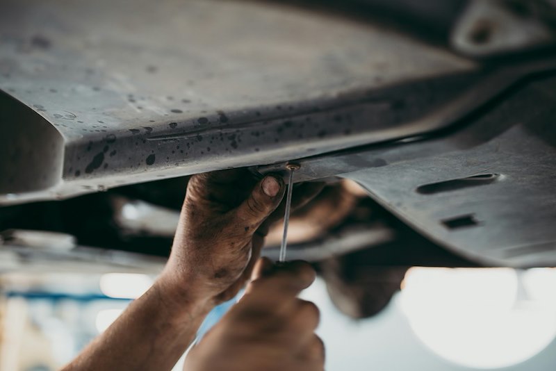 A mechanic prepares to drain an oil pan from under a vehicle
