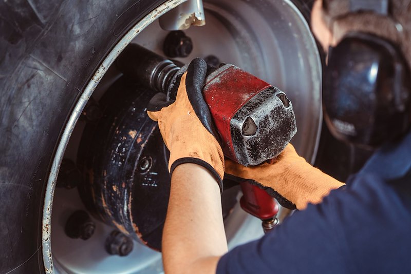 A mechanic in blue shop clothes reattaches a brake rotor with a red impact wrench.