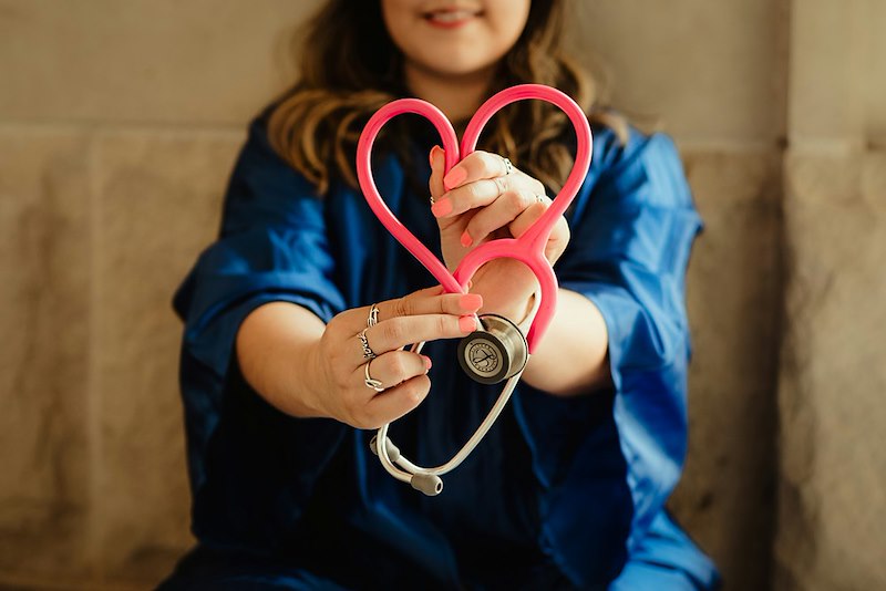 A nurse holds up her stethoscope in a heart.