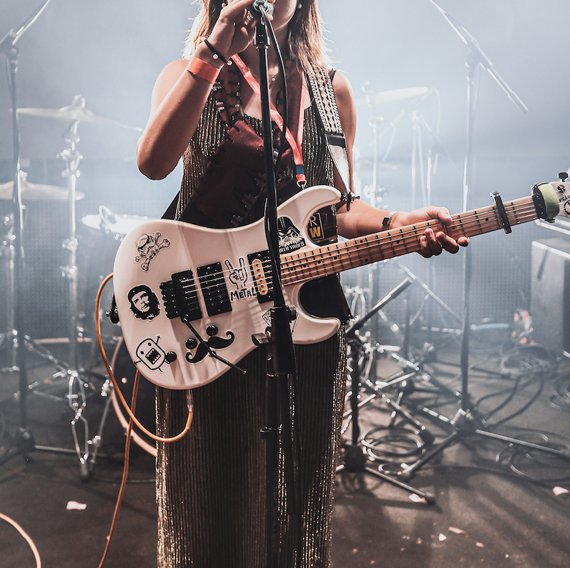 A punk rocker stands on stage at a microphone while holding her guitar