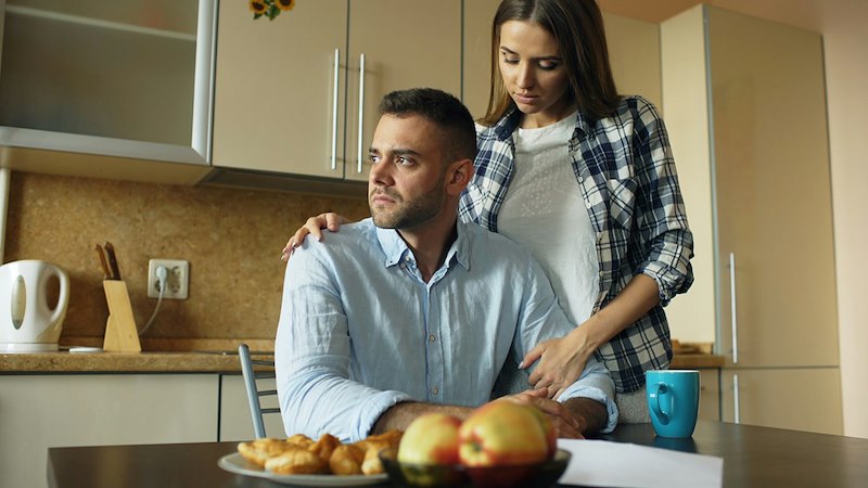 A woman comforts a man at a table with produce